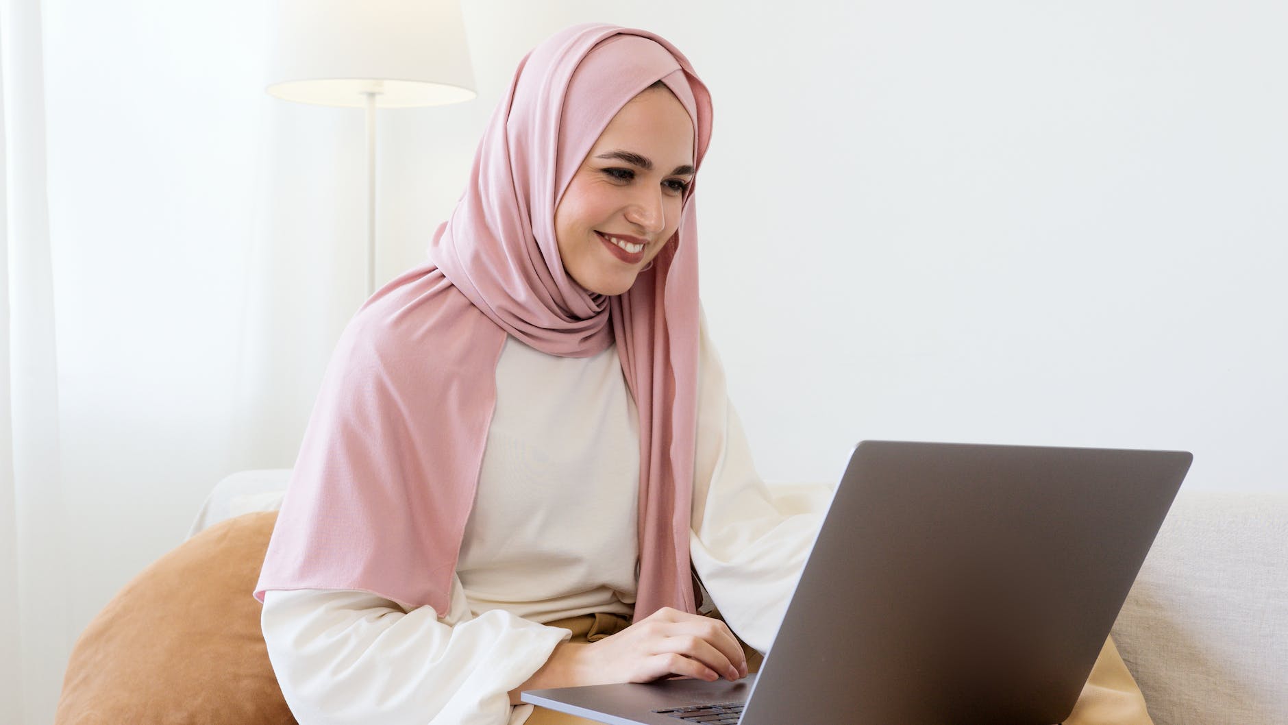 woman in pink hijab and white long sleeve shirt using gray laptop