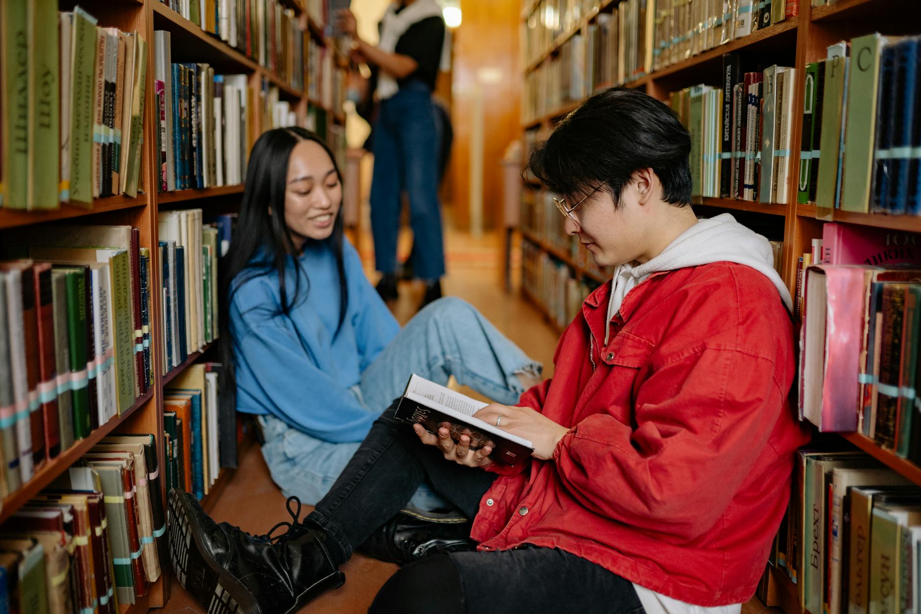 man in red jacket sitting on the floor beside woman in blue long sleeve shirt